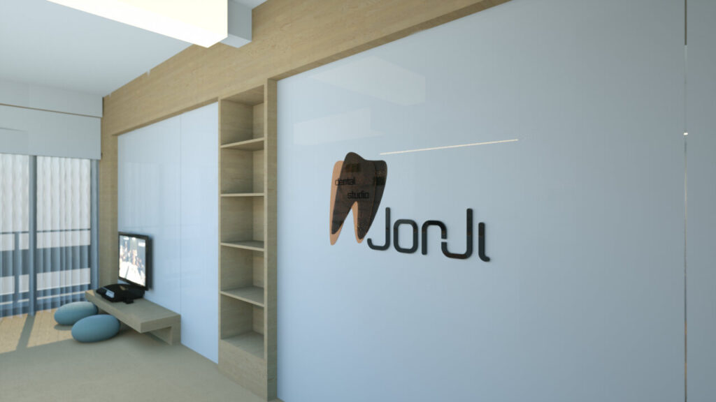 Modern interior design of a dental studio reception area featuring a white wall with a stylized tooth and "Jorji" logo, built-in wooden shelving, a light blue sofa, and a television, creating a clean and welcoming atmosphere. By Modify Architects