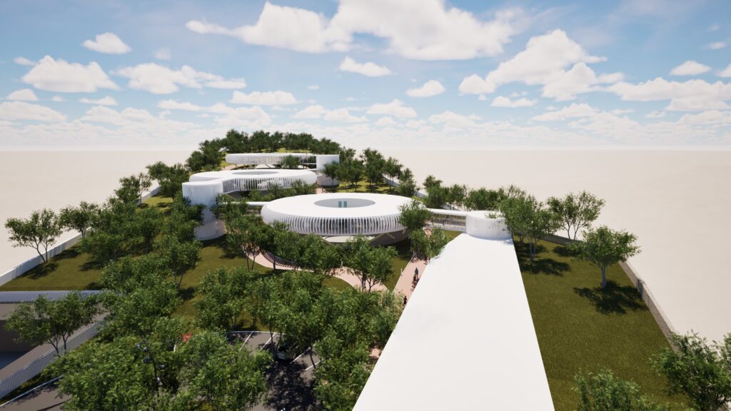 Aerial view of the "Education Rings" project, showcasing a modern school campus with circular buildings interconnected by white walkways, nestled within lush green landscaping and trees under a bright blue, cloudy sky. The design emphasizes a connection to nature and a flowing, open learning environment. By Modify Architects